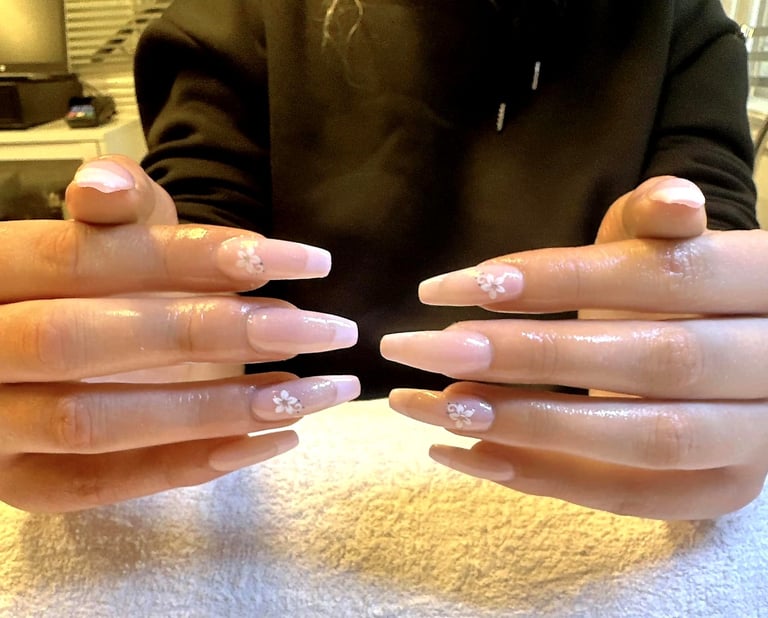 Hands displaying long white acrylic nails with pink floral nail art design over a yellow towel