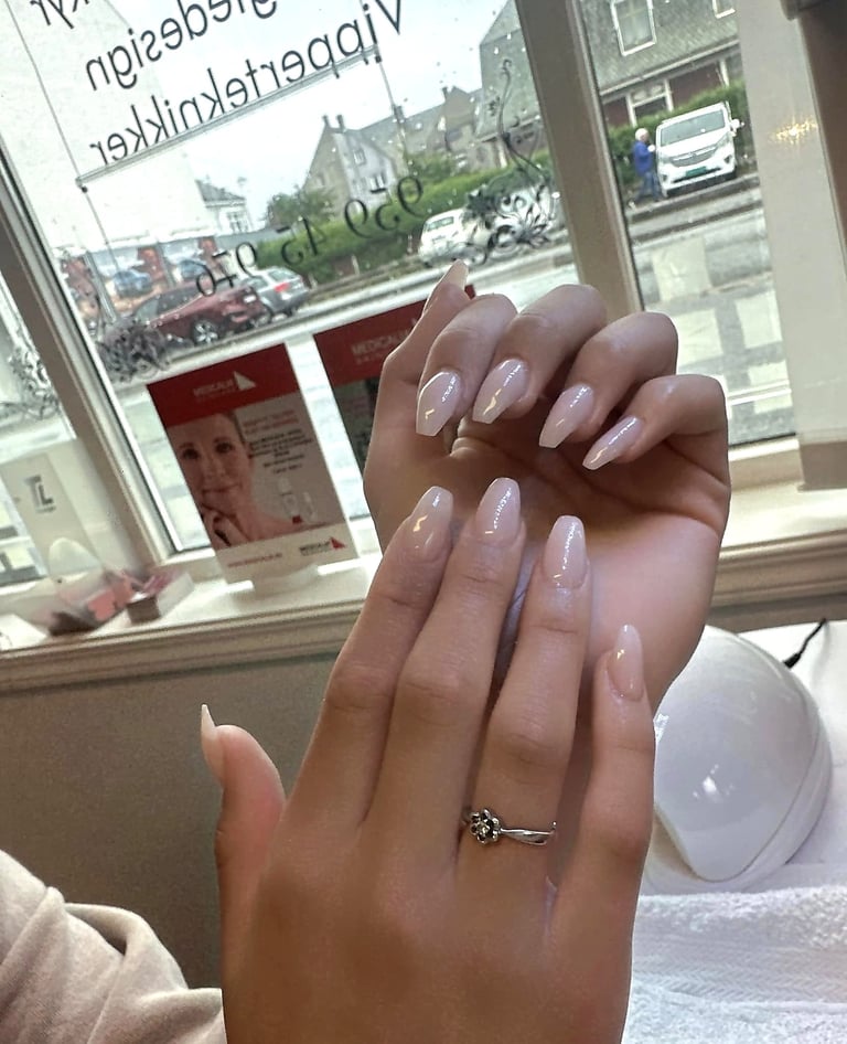 Close-up of a hand displaying long almond-shaped nails with a nude glitter manicure and a diamond ring