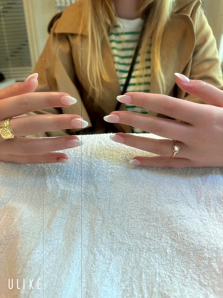 Woman displaying manicured nails with pink and white ombre design, wearing gold and diamond rings