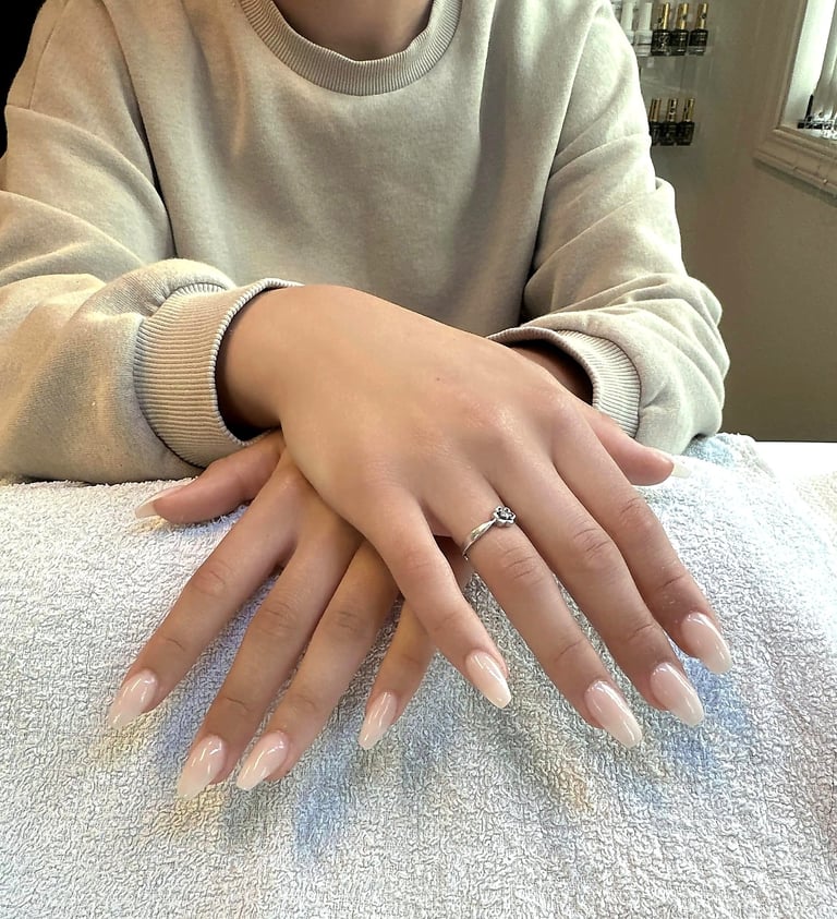 Person wearing cream sweater displaying manicured hands with nude almond-shaped nails and a diamond ring on white towel