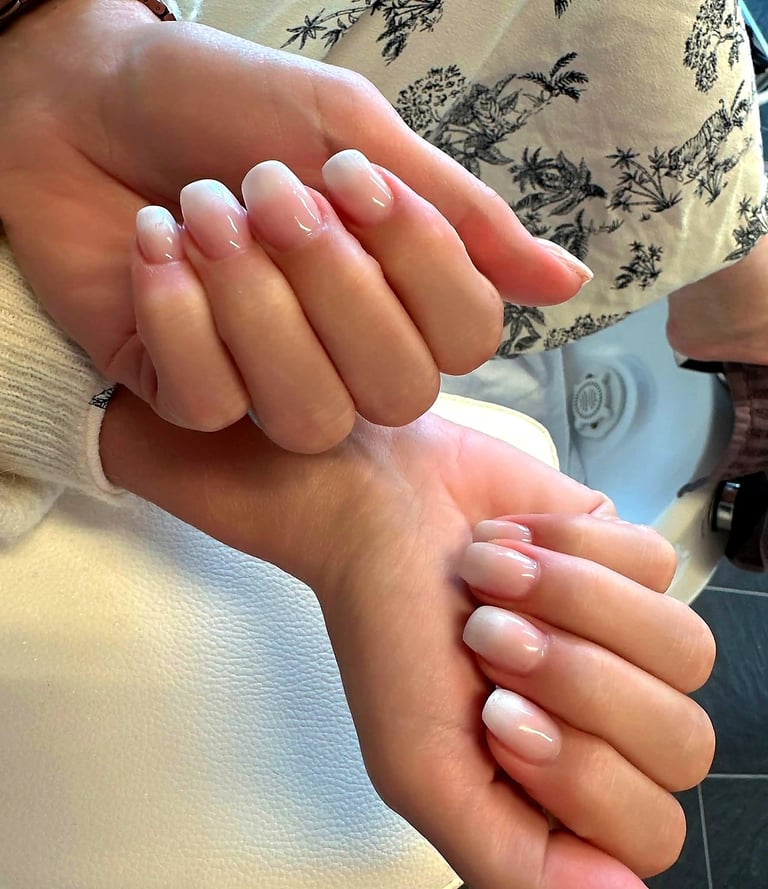 Close-up of two hands displaying manicured nails with natural pink and white ombre French tip design