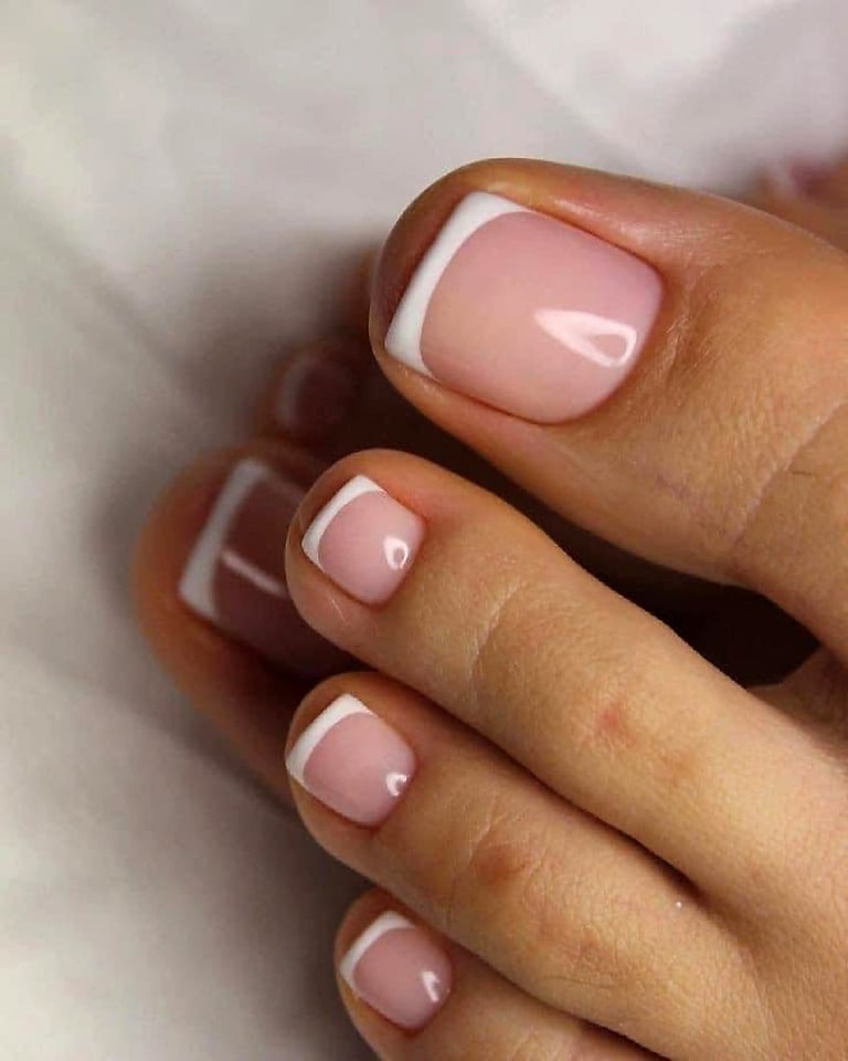 Close-up of manicured nails with soft pink polish and white French tip design on a light background